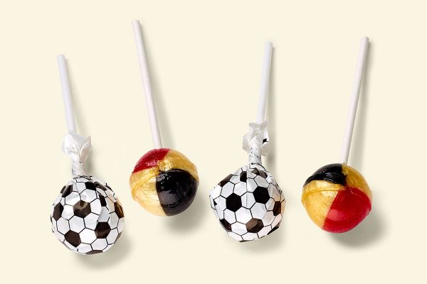 4 Küfa football lollies (ball shaped lollipops), of which 2 with wrapper (printed black and white football design) and two without wrapper, So you can see the colors of the lolly black, red and gold.